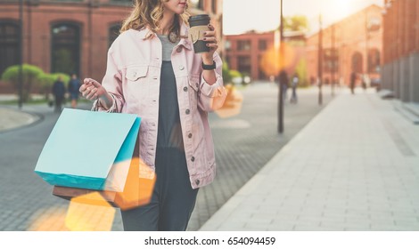 Close-up of paper bags in female hand.Young woman carries shopping bags and drinks coffee. Girl bought presents for her friends. Hipster girl has coffee break after shopping. In background cityscape. - Powered by Shutterstock