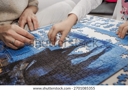 Close-up of parent and child assembling a jigsaw puzzle together at home. Family leisure activity, bonding, and teamwork concept