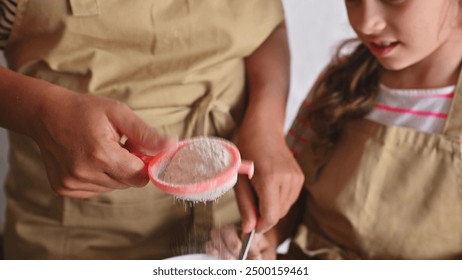 Close-up of a parent and child sifting flour and bonding as they bake together in the kitchen, showcasing family and culinary activities. - Powered by Shutterstock