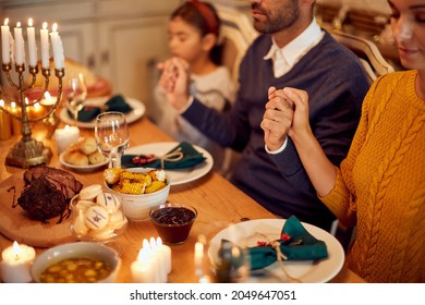 Close-up of parents and daughter holding hands and praying during family meal on Hanukkah. 