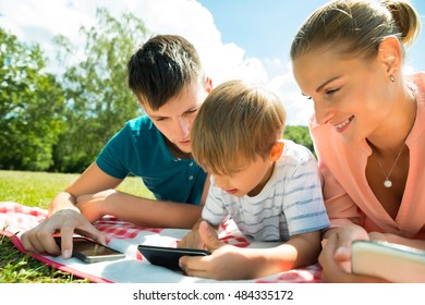 Close-up Of Parents Looking At Their Son Using Smartphone While Laying Down In The Park - Shutterstock ID 484335172