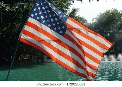 closeup part of fabric american flag with blue pool fountain in garden background