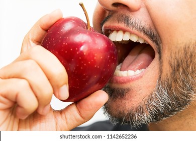 Nahaufnahme eines Teils des Gesichts eines bärtigen Mannes, der einen roten Apfel isst