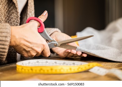 Close-up partial view of female hands citting fabric with scissors