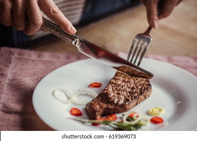 Close-up partial view of woman eating steak with fork and knife 
