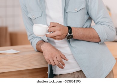 close-up partial view of young man holding white cup and drinking coffee