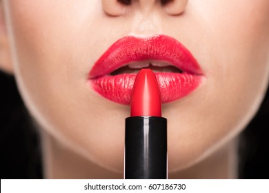Close-up partial view of young stylish woman applying red lipstick on black  