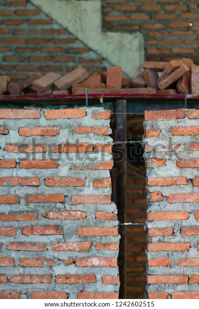 Closeup of partially laid red brick wall\
construction with mortar on residential project with bricks pile\
and reinforced concrete stair structure in the background.\
Traditional construction\
concept.