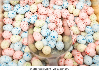 Close-up of pastel-colored speckled egg-shaped candies in a bulk bin with a clear plastic scoop, perfect for Easter or spring-themed settings - Powered by Shutterstock