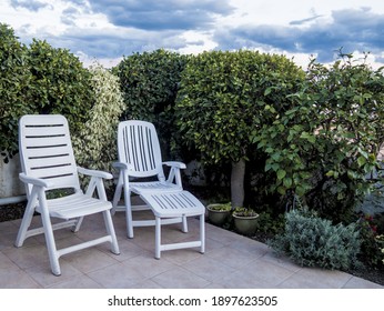 A Closeup Of Patio Furniture, Two Comfortable Plastic Loungers In The Beautiful Garden