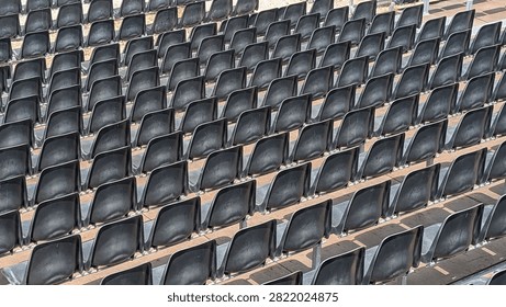 Close-up pattern of empty black plastic stadium seats arranged in diagonal rows, creating a repetitive geometric texture.