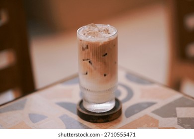Close-up of a patterned mosaic tile tabletop showcasing a refreshing iced beverage in a textured glass, capturing the casual, sunlit, and aesthetic vibe of a contemporary urban cafe interior