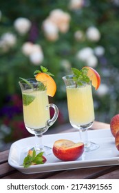 Closeup Of Peach Mojito Garnished With Peach Wedge And Twig Of Mint. Outside Cocktails, Drinks In A Garden.