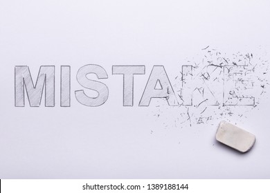 Close-up Of Pencil Eraser Erasing Mistake Word On White Paper