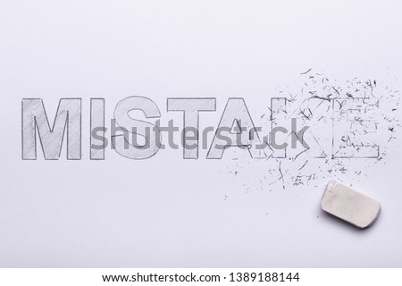 Close-up Of Pencil Eraser Erasing Mistake Word On White Paper