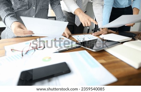 Close-up of people hands and important business paper lying on wooden table. Female hand holding sheet of paper. Man standing and pointing finger on tablet with empty screen