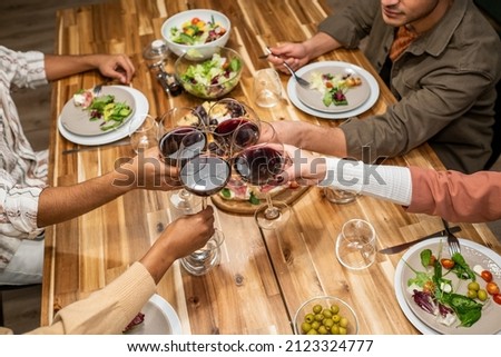 Close-up of people toasting with glasses of red wine while sitting at dining table with meal, they celebrating something at party