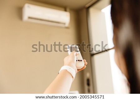 Closeup people using remote control adjust room temperature in home office pointing to Air conditioner in hot summer season.