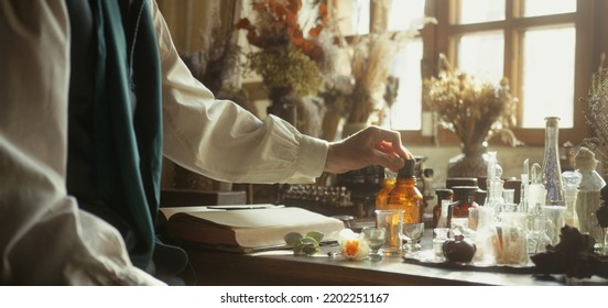 A close-up of a perfumer at his desk looking for a new fragrance. Vintage cinematic perfumery concept. Sunny day in the working workshop. Lots of ingredients, glass flasks. Depth of field