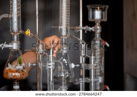 Close-up of a person adjusting a hydrometer inside a glass alcohol distillation apparatus in a laboratory setup.