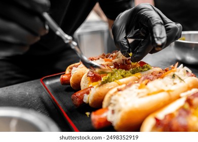 Close-up person in black attire and gloves preparing hot dogs with various toppings on black plate, highlighting the vibrant colors and textures of food. Perfect for culinary and street food themes - Powered by Shutterstock