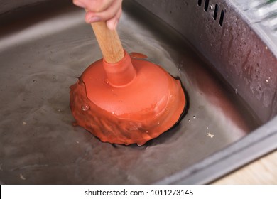 Close-up Of A Person Cleaning Sink Filled With Water With Cup Plunger