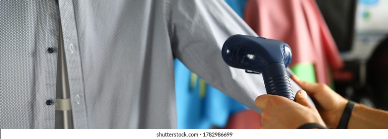 Close-up Of Person Cleans Grey Shirt With Special Nozzle On Clothing Steamer. Worker Preparing Clothing For Selling. Ironing Jacket. Fashion Store And Business Concept