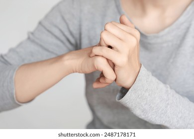 Close-up of a person cracking their knuckles. The image shows hands in action, wearing a grey long-sleeved shirt against a plain background. - Powered by Shutterstock