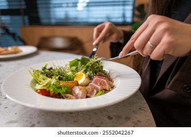 A close-up of a person enjoying a vibrant salad, featuring fresh greens, cherry tomatoes, and a soft-boiled egg. The setting is modern and inviting, perfect for a healthy meal. - Powered by Shutterstock