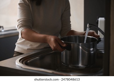 Close-up of a person filling a pot with water at a kitchen sink, capturing a daily household chore. - Powered by Shutterstock