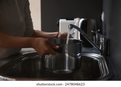 Close-up of a person filling a pot with water at a kitchen sink. Concept of household chores and daily life activities. - Powered by Shutterstock