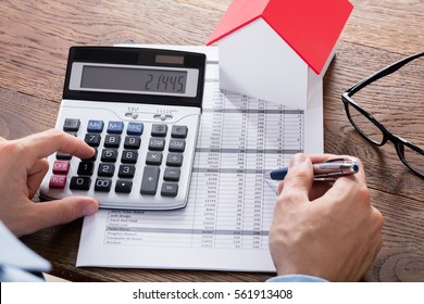 Close-up Of A Person Hand Calculating A Real Estate Property Tax On Wooden Desk
