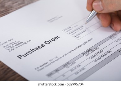 Close-up Of A Person Hand Filling A Purchase Order Form On Wooden Desk