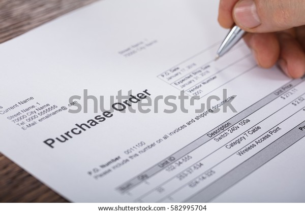 Close-up Of A Person Hand Filling A Purchase Order\
Form On Wooden Desk