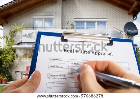 Close-up Of Person Hand Filling Real Estate Appraisal Document In Front Of House