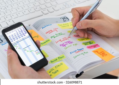Close-up Of Person Hands With Mobile Phone And List Of Work In Diary - Powered by Shutterstock