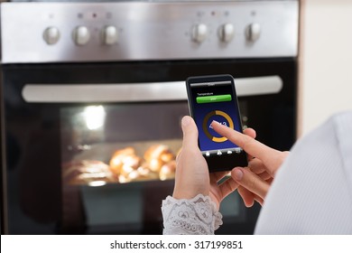 Close-up Of Person Hands Operating Oven Appliance With Mobile Phone