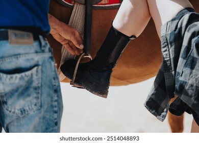 Close-up of a person helping a rider adjust the stirrup while mounting a horse, emphasizing teamwork and equestrian preparation. - Powered by Shutterstock