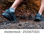 A close-up of a person hiking through a muddy forest trail wearing black sneakers and gray socks