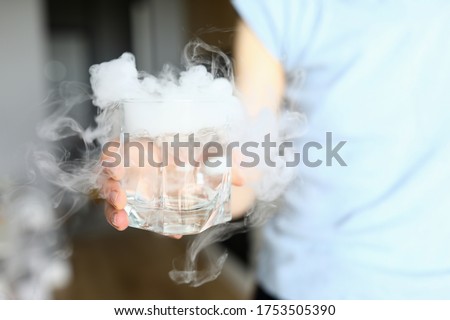 Close-up of person holding glass with water and cubes of dry ice. Cold summer drink. Mans hand and liquid. Cooling beverage and impressive effect concept