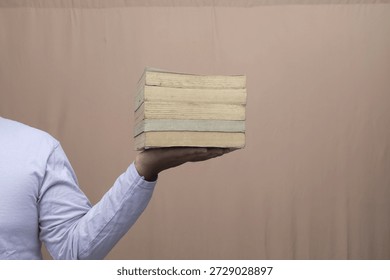 Close-up of person holding thick stack of worn books on open palm against plain background