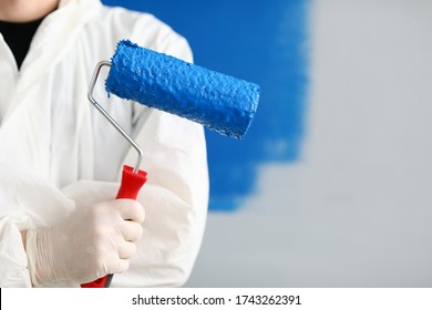 Close-up of person painter holding roller covered in blue paint. Professional worker wearing protective uniform and gloves. Copy space in right side. Renovation concept