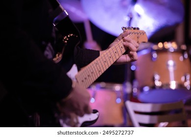 Close-up of a person playing an electric guitar with drum set in the blurred background. Focus on the guitar neck and hands. - Powered by Shutterstock