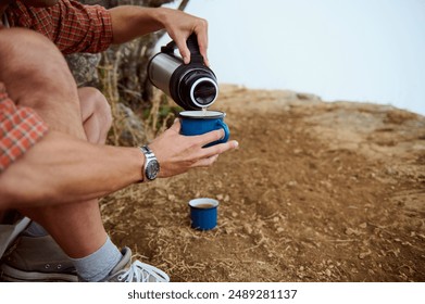 Close-up of a person pouring hot beverage from a thermos into a blue cup outdoors. Relaxation, adventure, and nature concepts. - Powered by Shutterstock