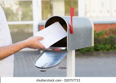 Close-up Of Person Putting Stack Of Letters In Mailbox
