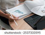 Close-up of a person reviewing financial charts and graphs on paper and a laptop, highlighting data analysis and business strategy.