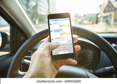 Close-up Of A Person Sending A Text Message Using Mobile Phone While Driving A Car