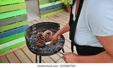 Close-up of a person setting up a grill with pinecones on a patio. The scene captures outdoor preparation with colorful wooden decor. - Powered by Shutterstock