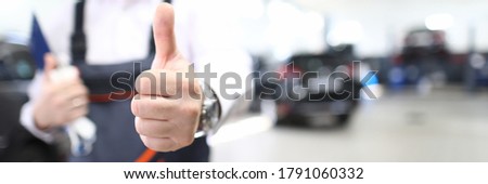 Close-up of person showing thumbs up. Good job and well done symbol. Copy space in right side. Mechanic in uniform posing in garage. Repair service station and handyman concept