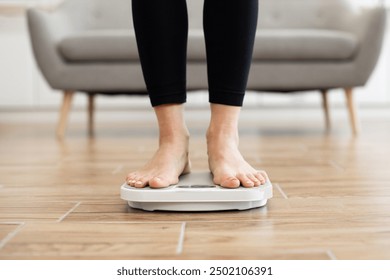 Close-up of person standing on digital bathroom scale in cozy living room setting. Focus on feet and legs, promoting healthy living, weight management, and fitness goals. - Powered by Shutterstock